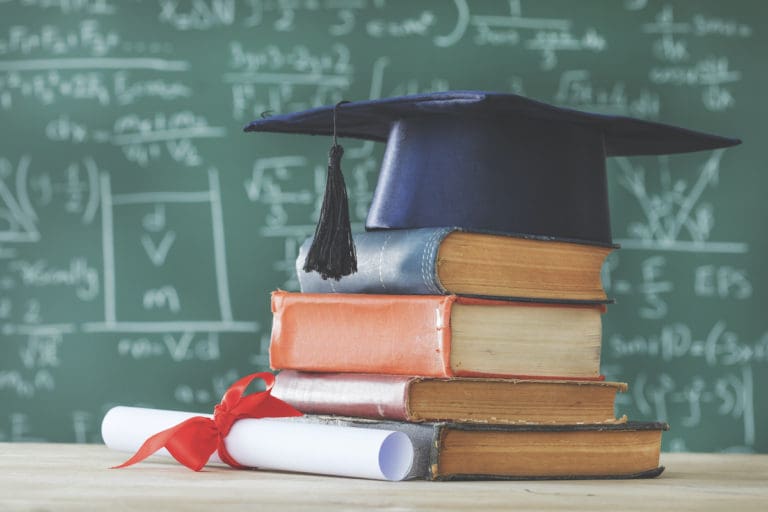 Stack books  graduate hat and diploma in front of  green chalkboard