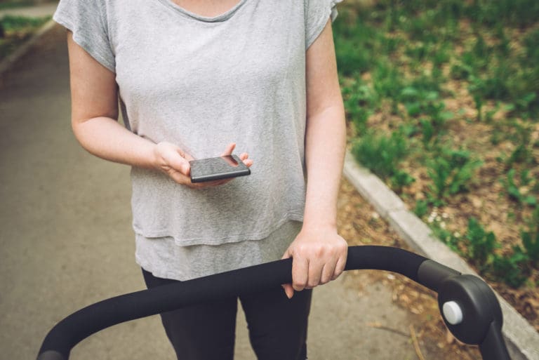 Mother pushing baby stroller and reading text message on smartph