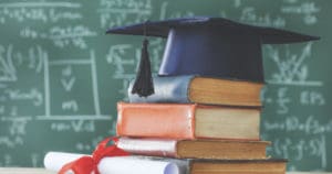 Stack books  graduate hat and diploma in front of  green chalkboard